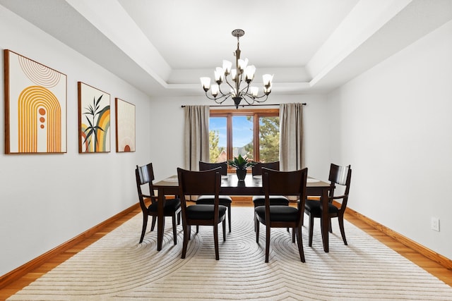 dining room featuring a raised ceiling, baseboards, light wood finished floors, and an inviting chandelier