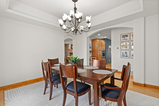 dining area featuring arched walkways, a notable chandelier, light wood-style flooring, and a tray ceiling