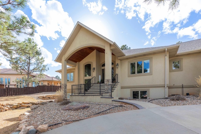 view of front of home with a shingled roof, fence, and stucco siding