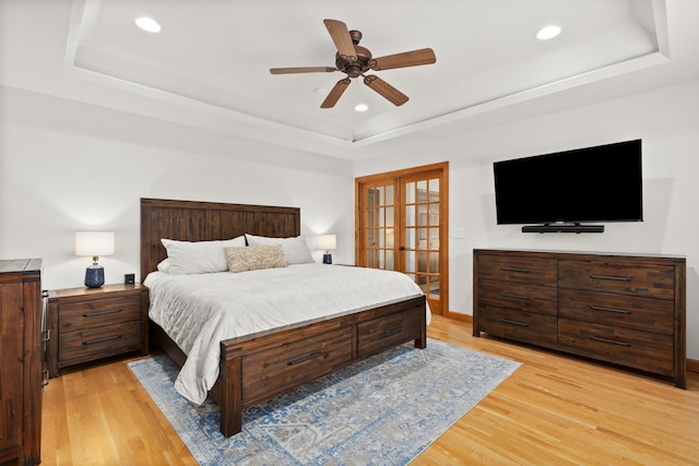 bedroom with light wood finished floors, french doors, a tray ceiling, and recessed lighting