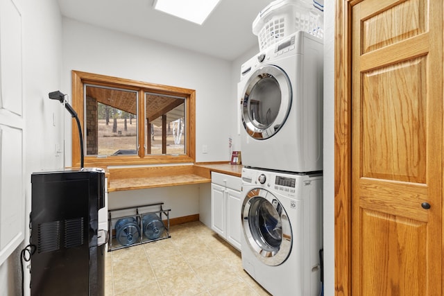 laundry area with light tile patterned floors, stacked washer and dryer, cabinet space, and baseboards