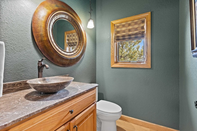 half bathroom featuring toilet, a textured wall, vanity, and baseboards