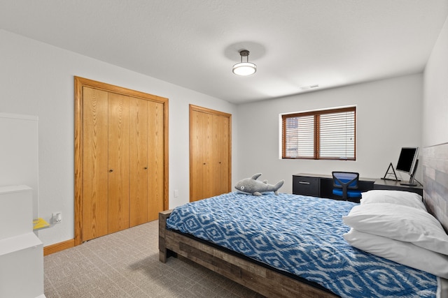 carpeted bedroom with two closets, visible vents, and baseboards