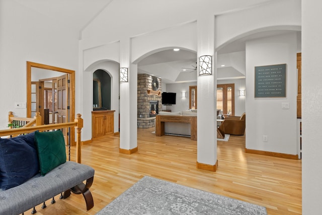 living room featuring ceiling fan, arched walkways, a large fireplace, wood finished floors, and baseboards