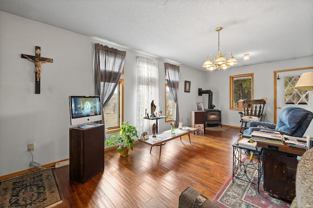 interior space with an inviting chandelier, a wood stove, a textured ceiling, wood finished floors, and baseboards