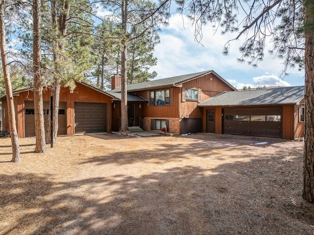 view of front of property with brick siding, an attached garage, a chimney, and dirt driveway