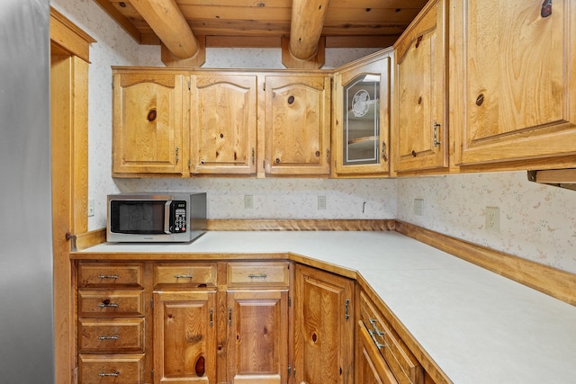 kitchen featuring wood ceiling, glass insert cabinets, stainless steel microwave, light countertops, and beam ceiling