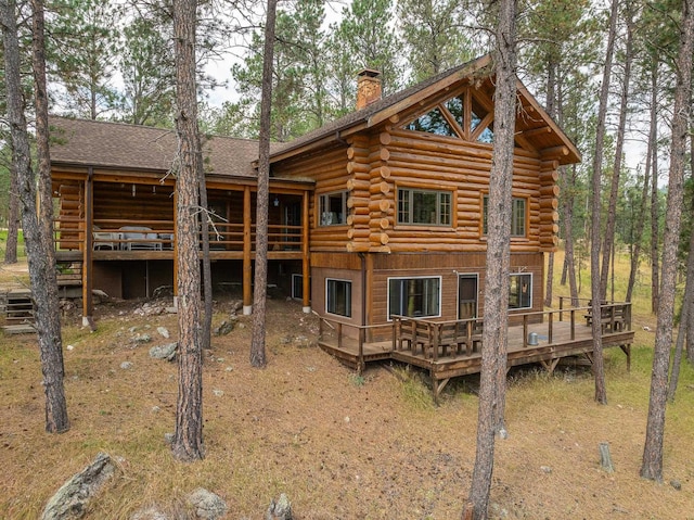 rear view of house featuring a deck, a chimney, and log siding