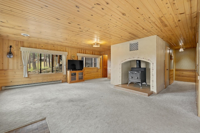 unfurnished living room with visible vents, wood ceiling, a wood stove, carpet, and a baseboard heating unit