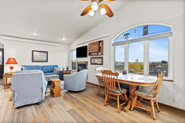 living area featuring high vaulted ceiling, a glass covered fireplace, ceiling fan, and light wood-style flooring