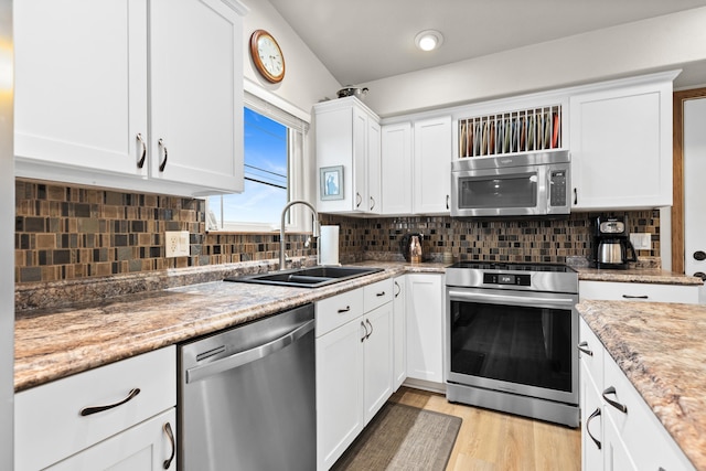 kitchen featuring tasteful backsplash, white cabinets, stainless steel appliances, light wood-type flooring, and a sink