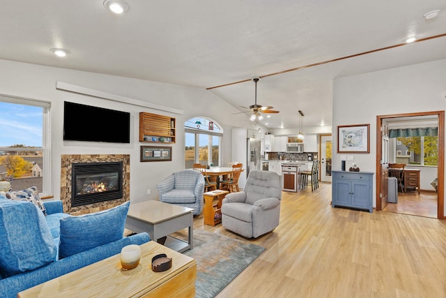 living area with a fireplace, a healthy amount of sunlight, vaulted ceiling, and light wood finished floors