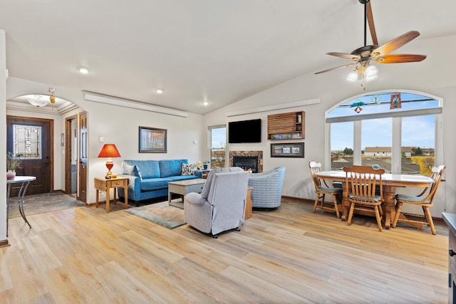 living room featuring arched walkways, a lit fireplace, light wood finished floors, and vaulted ceiling