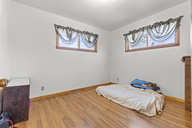 bedroom with multiple windows, visible vents, baseboards, and wood finished floors