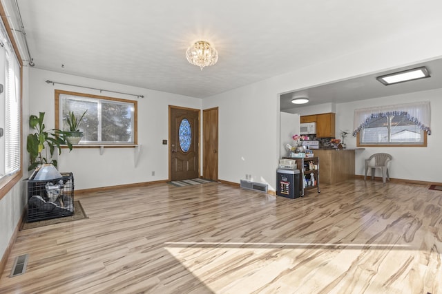 foyer with light wood-style flooring, an inviting chandelier, visible vents, and baseboards