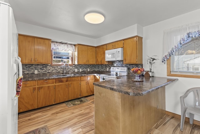 kitchen featuring white appliances, brown cabinetry, dark countertops, a peninsula, and a sink