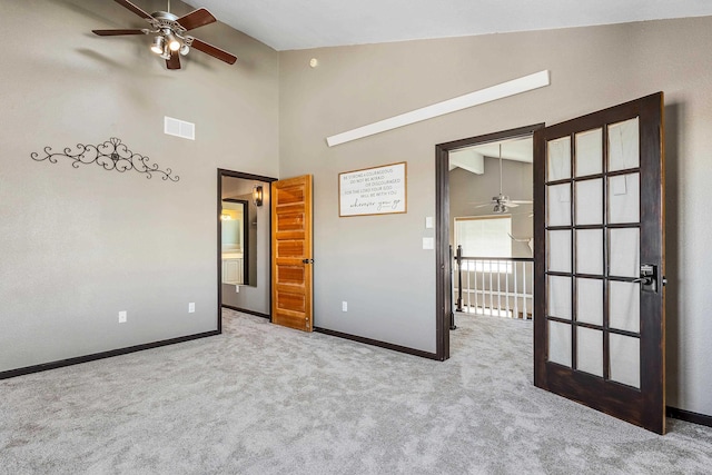 carpeted empty room with high vaulted ceiling, visible vents, baseboards, and a ceiling fan