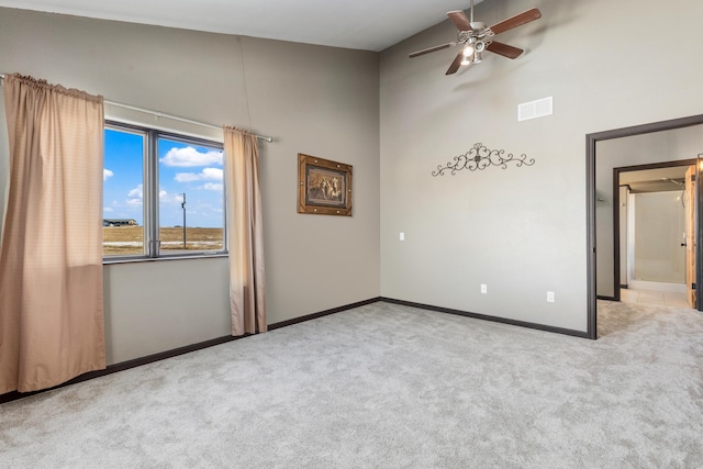 carpeted empty room featuring a ceiling fan, a towering ceiling, visible vents, and baseboards