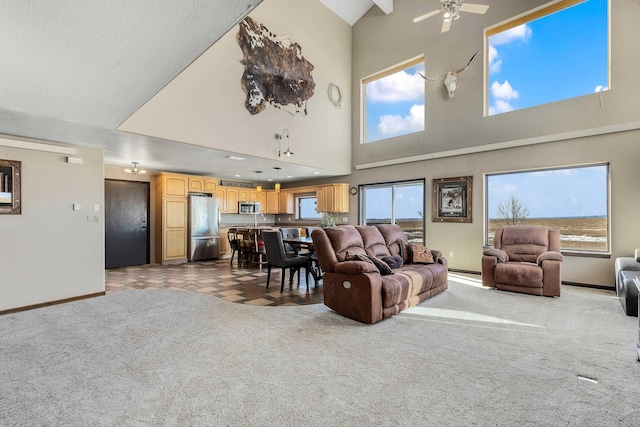 living area with a towering ceiling, a ceiling fan, baseboards, and carpet flooring