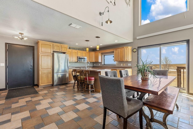 dining area featuring visible vents, a towering ceiling, a textured ceiling, stone tile flooring, and recessed lighting