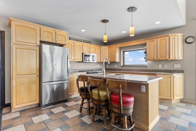 kitchen featuring stainless steel appliances, a kitchen island with sink, a sink, and light brown cabinetry