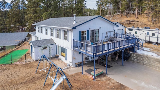 back of house featuring an outbuilding, roof with shingles, fence, a deck, and a patio area