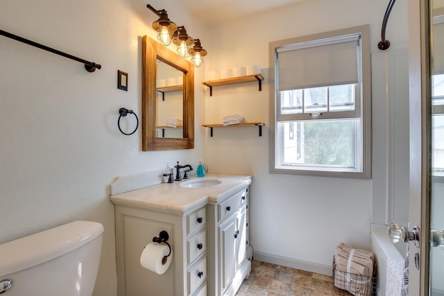 bathroom featuring toilet, stone finish flooring, baseboards, and vanity