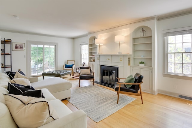 living area with ornamental molding, plenty of natural light, a fireplace with flush hearth, and light wood-style flooring