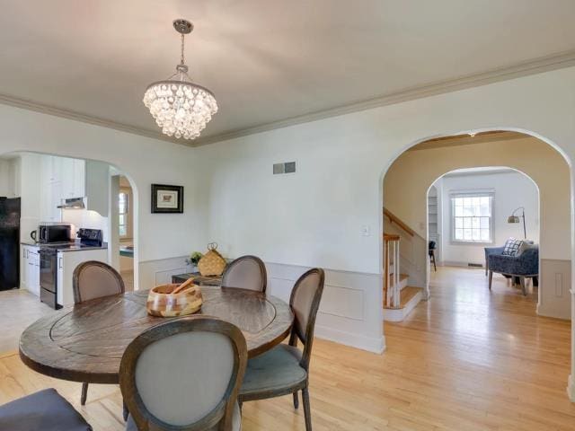 dining space featuring a chandelier, light wood-type flooring, a wainscoted wall, and visible vents