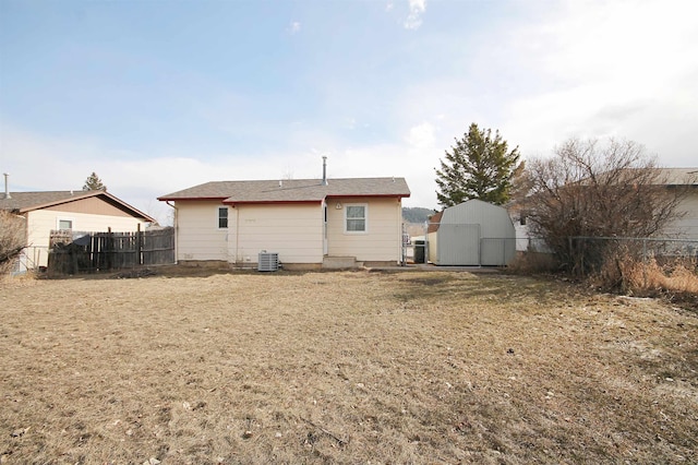 rear view of house featuring a storage shed, central AC unit, a lawn, an outbuilding, and fence