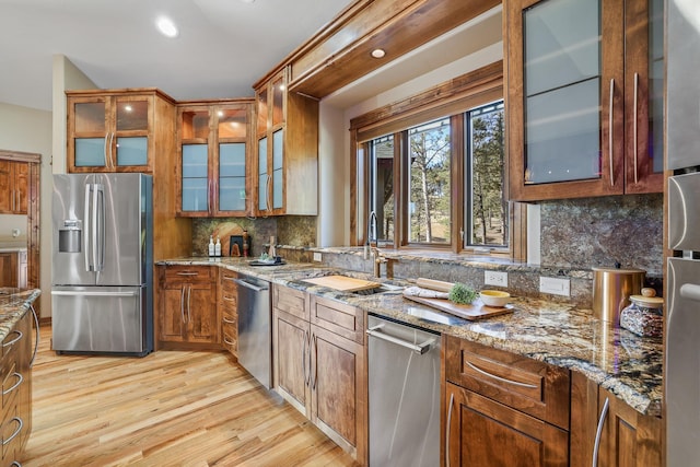 kitchen featuring a sink, appliances with stainless steel finishes, light wood-type flooring, light stone countertops, and tasteful backsplash