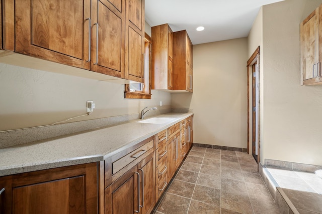 kitchen featuring light stone counters, brown cabinets, a sink, and baseboards