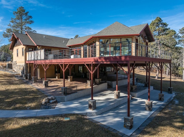 rear view of property with a shingled roof, stone siding, a patio area, and a deck