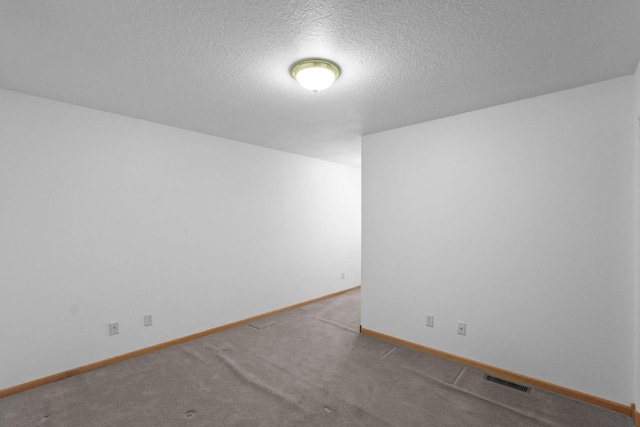 empty room featuring carpet floors, visible vents, a textured ceiling, and baseboards