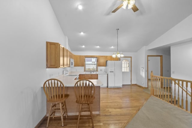 kitchen featuring light countertops, hanging light fixtures, light wood-style floors, white appliances, and a peninsula