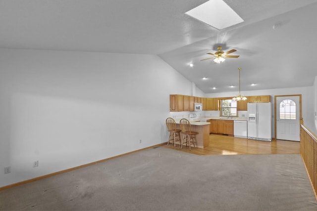 kitchen with light colored carpet, light countertops, vaulted ceiling with skylight, white appliances, and a peninsula