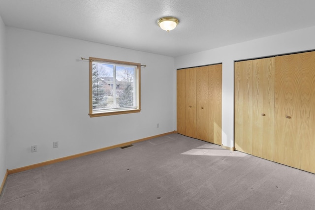 unfurnished bedroom with baseboards, visible vents, carpet, a textured ceiling, and multiple closets