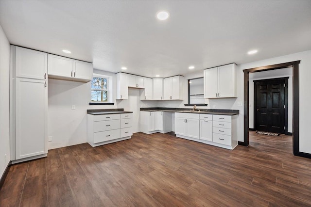 kitchen with dark wood-style flooring, dark countertops, recessed lighting, white cabinetry, and a sink