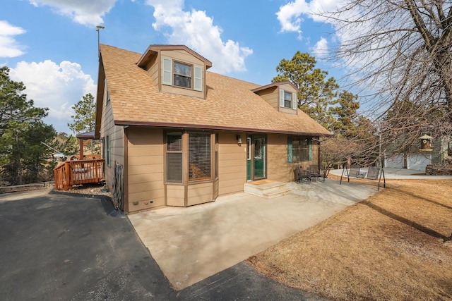 view of front of home featuring a deck, a patio, and roof with shingles