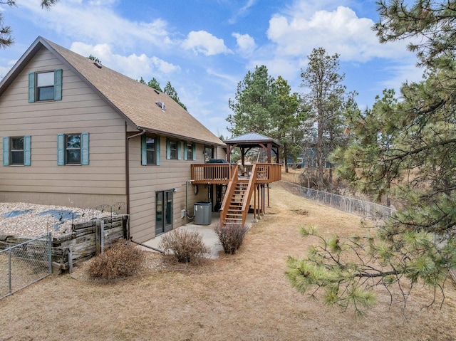 rear view of property featuring a fenced backyard, stairway, a shingled roof, and a gazebo