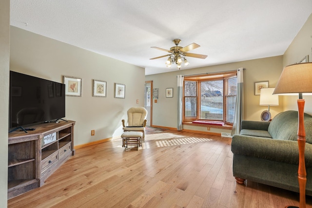 living area with light wood-style floors, visible vents, ceiling fan, and baseboards