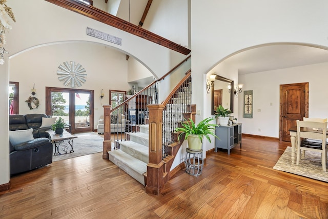 stairs featuring arched walkways, a high ceiling, wood finished floors, baseboards, and french doors