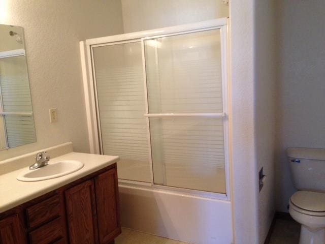 bathroom featuring combined bath / shower with glass door, vanity, and toilet