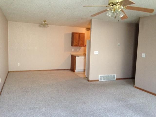 unfurnished living room with baseboards, visible vents, a ceiling fan, light colored carpet, and a textured ceiling