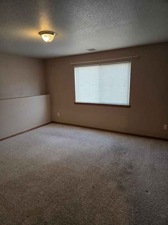 spare room featuring carpet floors, baseboards, visible vents, and a textured ceiling