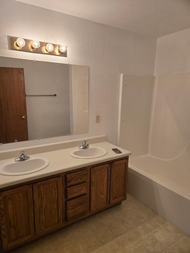 full bathroom featuring a textured wall, a sink, a textured ceiling, and double vanity