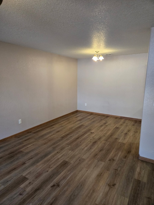 empty room with a textured ceiling, a chandelier, visible vents, baseboards, and dark wood-style floors