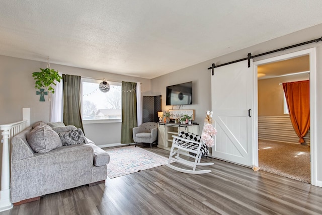 living area with a barn door, a textured ceiling, baseboards, and wood finished floors