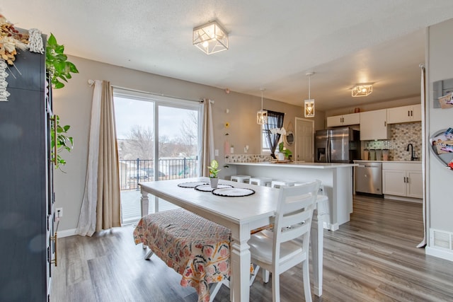 dining room featuring visible vents, a textured ceiling, light wood-style flooring, and baseboards