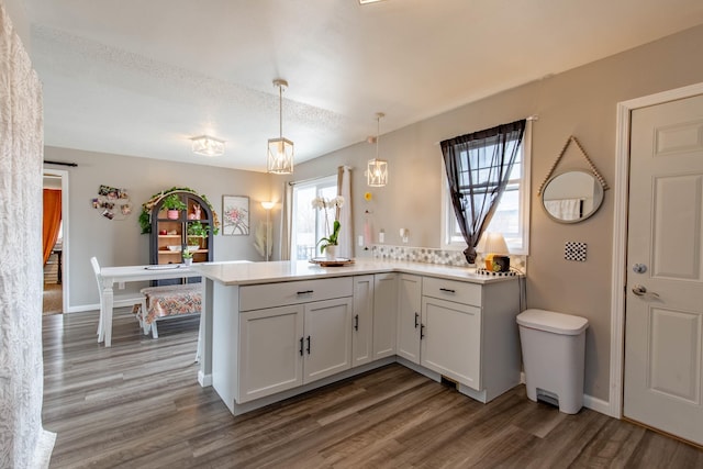 kitchen featuring pendant lighting, light countertops, white cabinetry, wood finished floors, and a peninsula